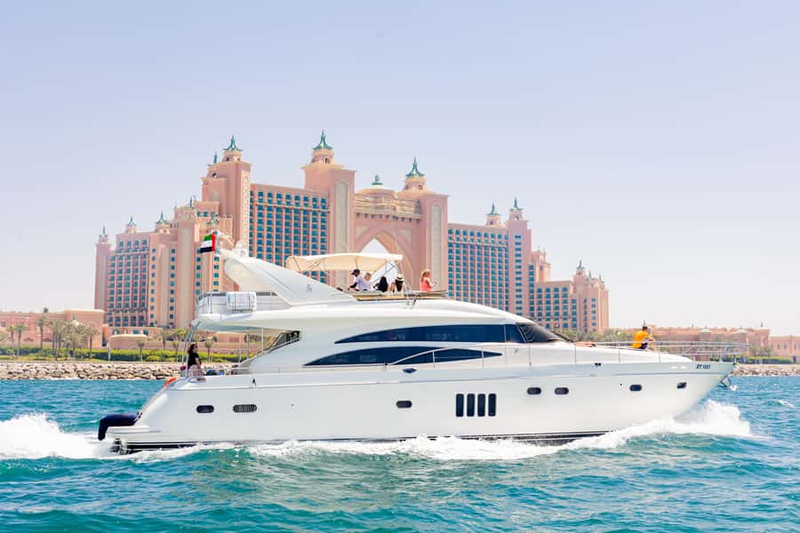 A white motor yacht running past the Palm on a flat blue morning in Dubai